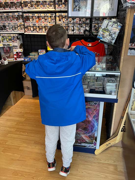 In side, our store image focuses on a boy standing at a glass case. He is looking through Pokémon cards