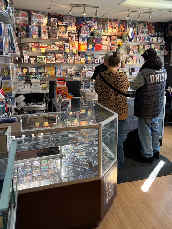 Inside shot of our store with a focus on two customers standing at the counter wanting to trade in collectible cards